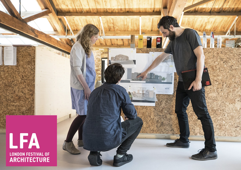 Three members of the Architype team stand in the light and airy London office. Surrounded by natural timber, they point at a housing scheme render attached to a cork board. The logo in the corner reads 'LFA London Festival of Architecture.'